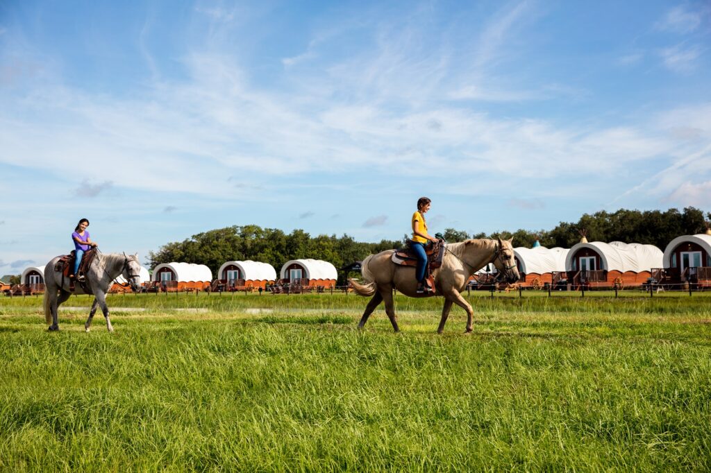 2 girls horseback riding in front of conestoga wagons at westgate river ranch resort and rodeo