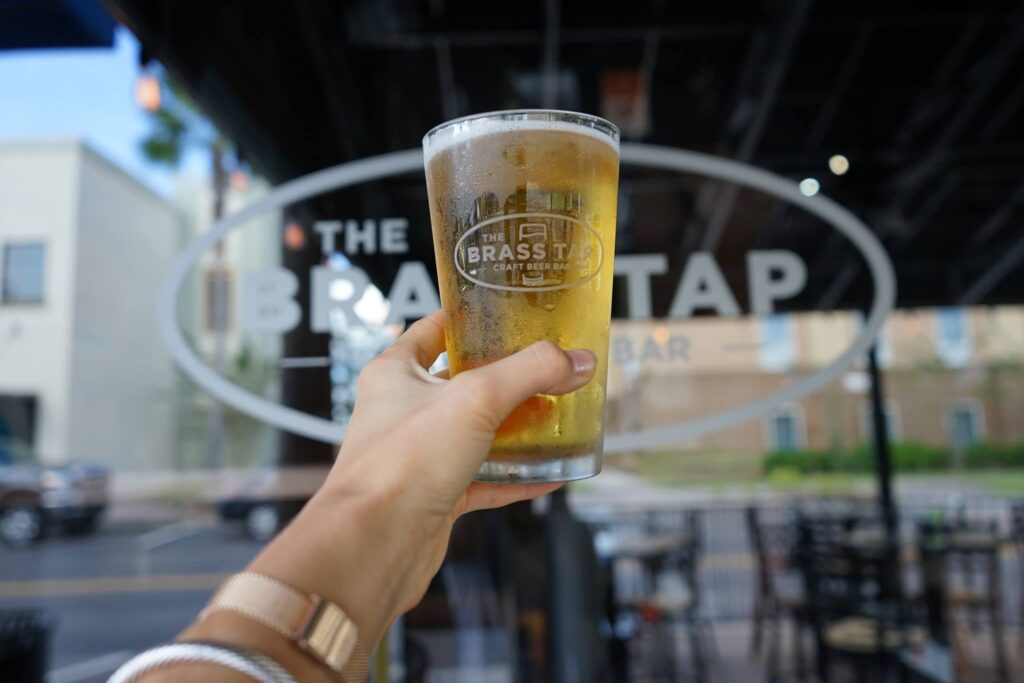 person holding a pint of beer at brass tap in lakeside village