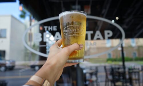person holding a pint of beer at brass tap in lakeside village