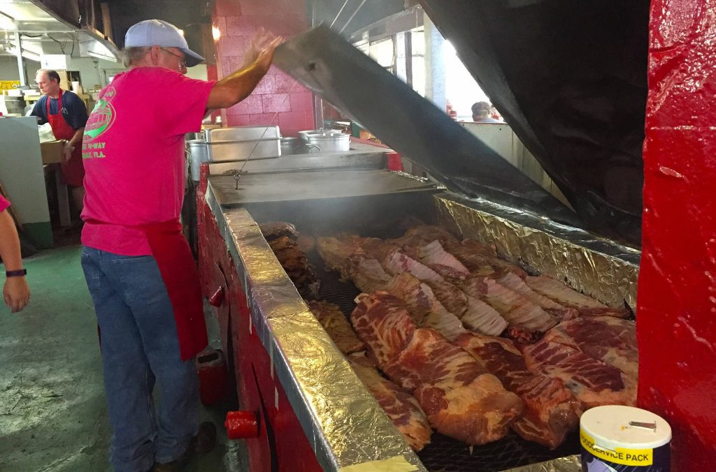 Man looking at racks of ribs cooking inside barbecue pit at Peebles Bar-B-Q in Auburndale, FL