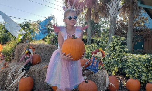 child holding pumpkin outside of Central Florida Visitor Information Center during Ghosts, Goblins, & Goodies