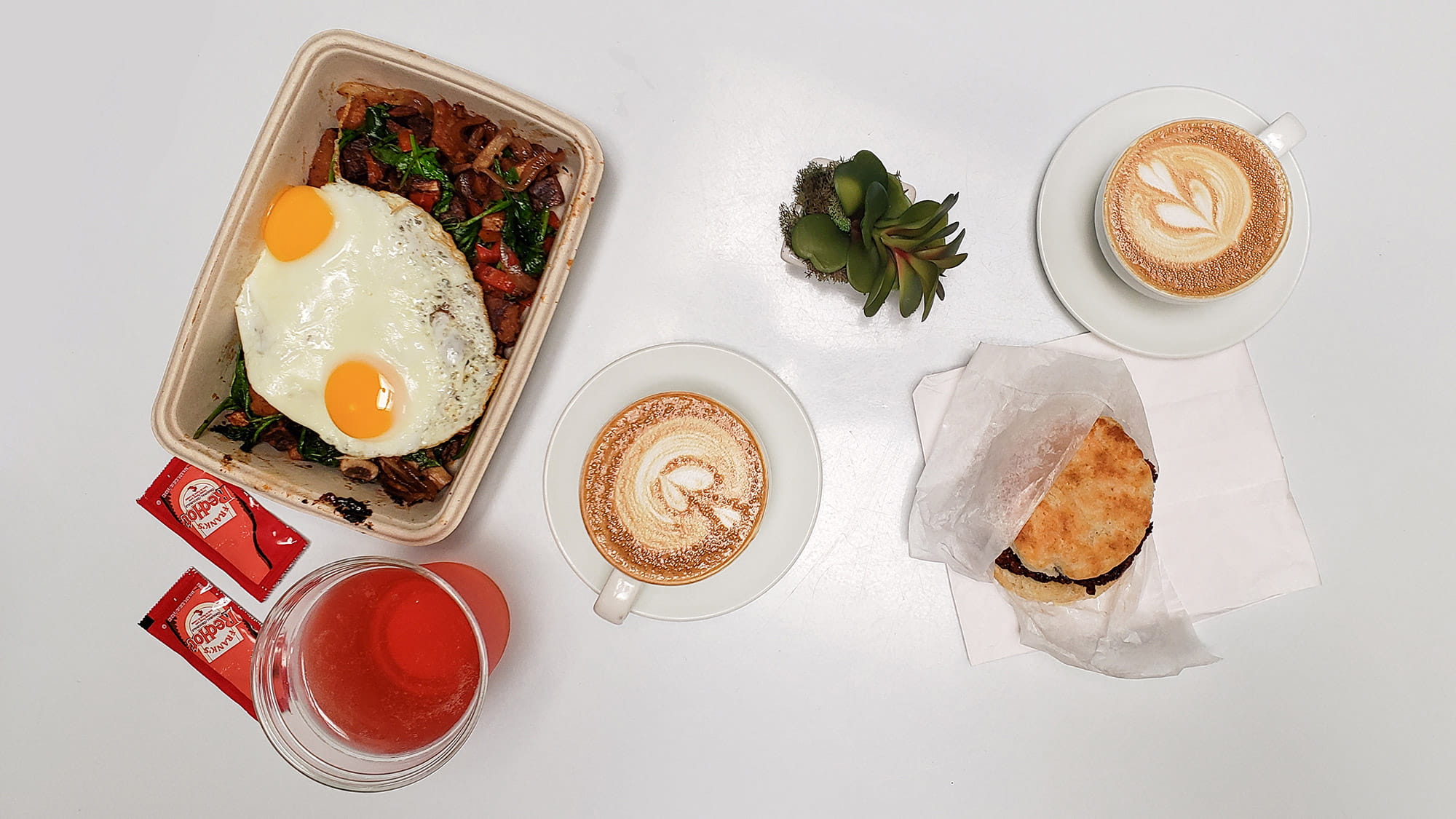 Food on white table. Vegan power bowl with two eggs, a chicken biscuit and Kombucha from Good Thyme LKLD. Two lattes from Concord Coffee.
