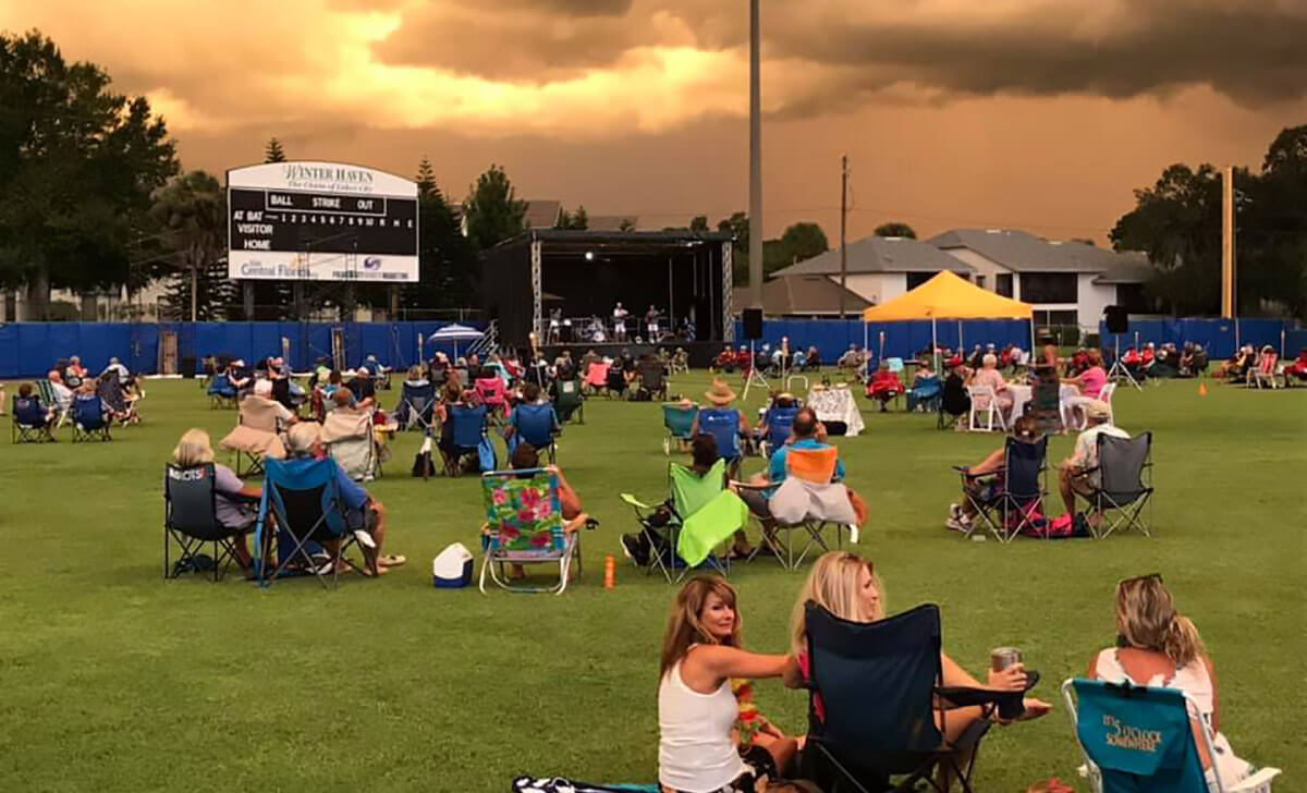 groups of people sitting outside at sunset during a concert at Chain O Lakes stadium